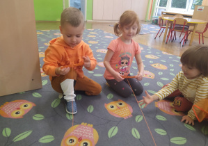 Dzieci owijają patyczek pomarańczową włóczką z klockiem
